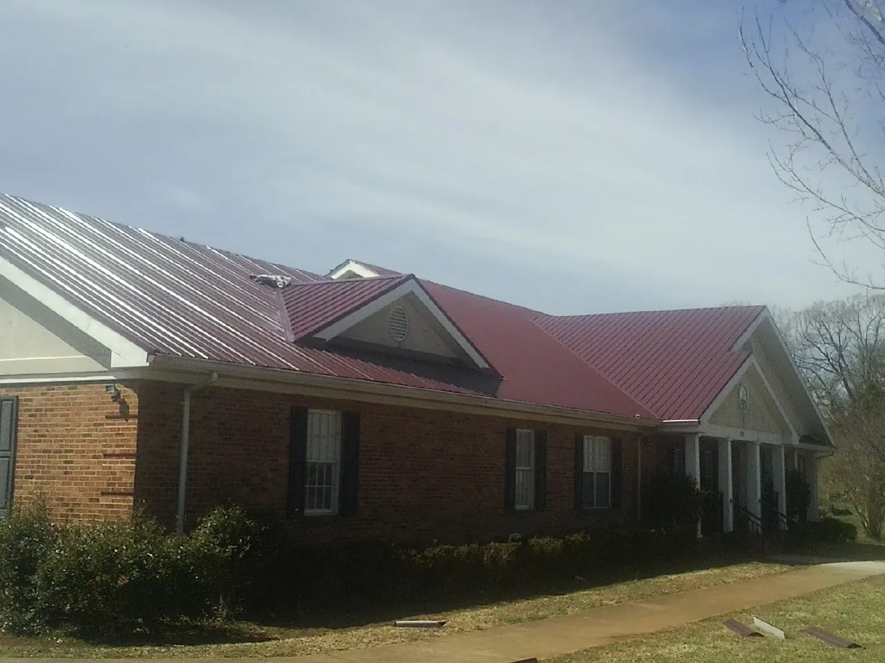 Red metal roof with gabled entries on a long brick building, from a Hail Damage Roof Repair job in Barrington